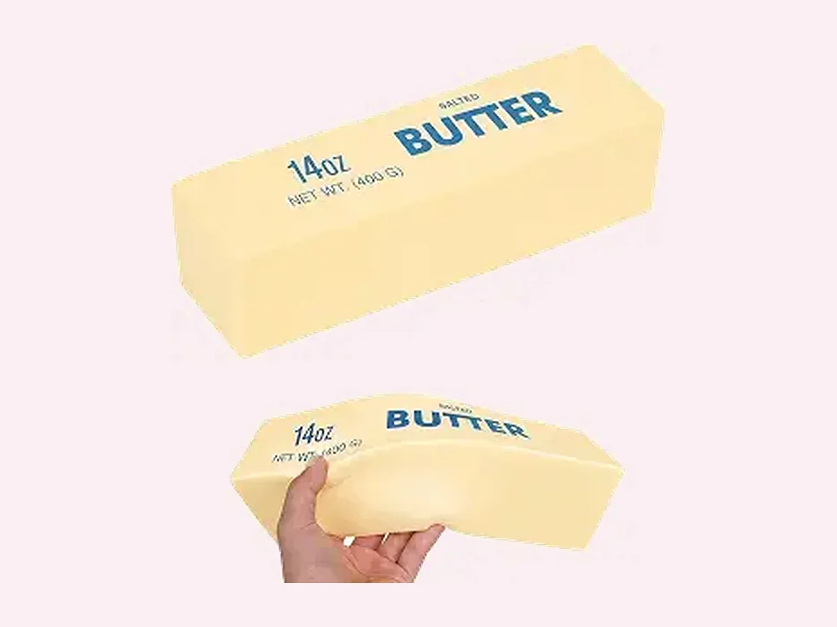 Folded pale-yellow butter bar squishy on a blush pink podium